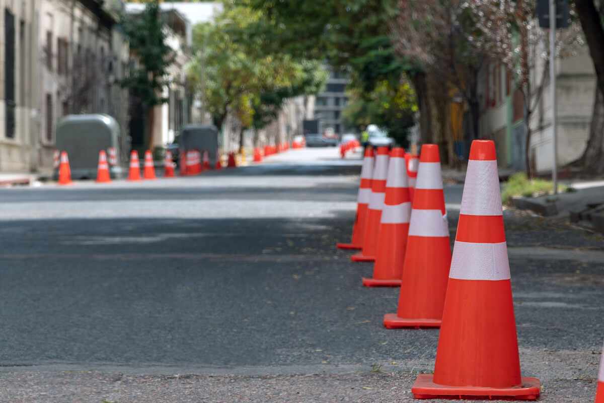 Row of orange traffic cones with white reflective stripes lining a city street, indicating a construction or roadwork zone.